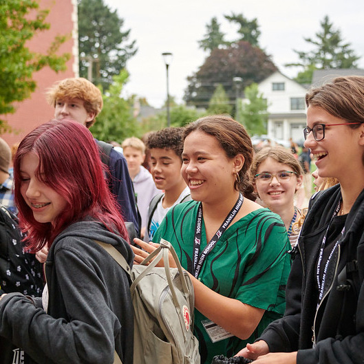 A group of smiling teens with backpacks walk together outside their school.