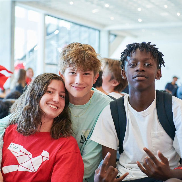 Three middle-school friends pose together—one in a red shirt, one in light green, and one in white—smiling for the photo.